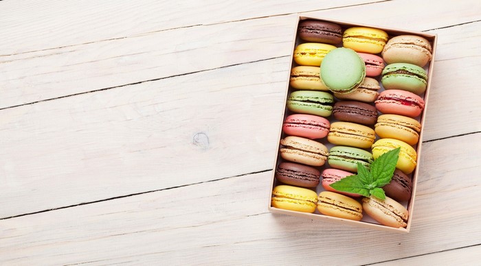 Box of colorful macarons with mint leaves on a wooden surface