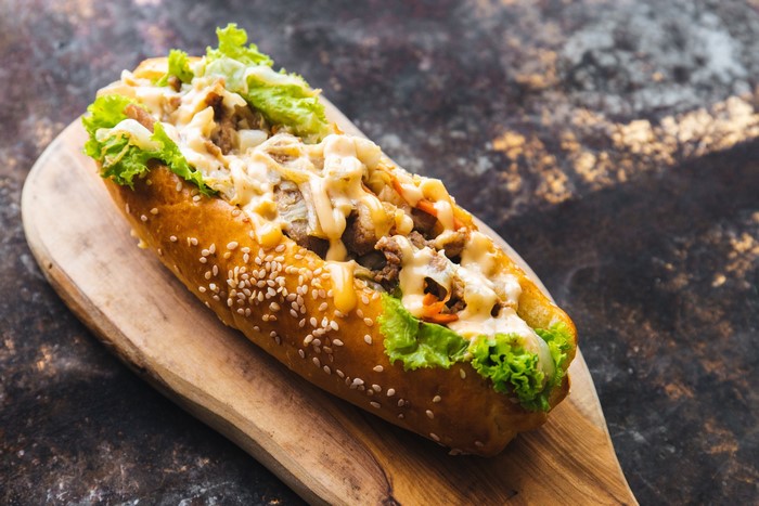 Hot dog with meat, lettuce, and cheese on a bun