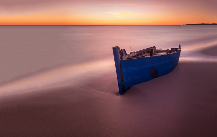 Blue boat on a sandy beach at sunset