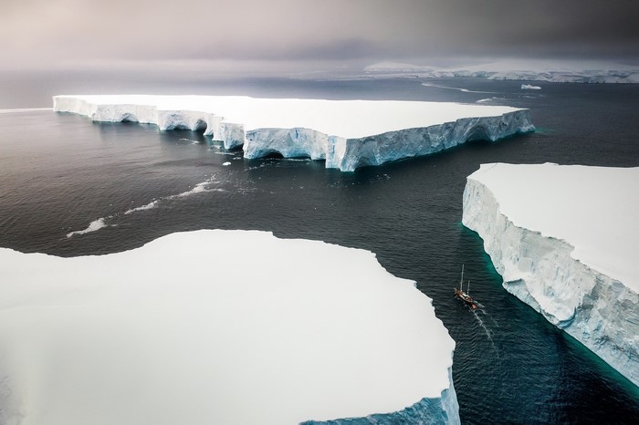 Sailboat navigates between icebergs in the Arctic sea