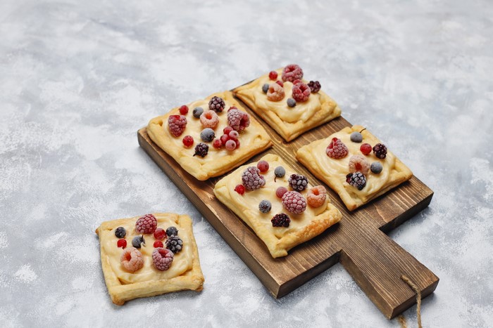 Puff pastry squares with cream and berries on a cutting board