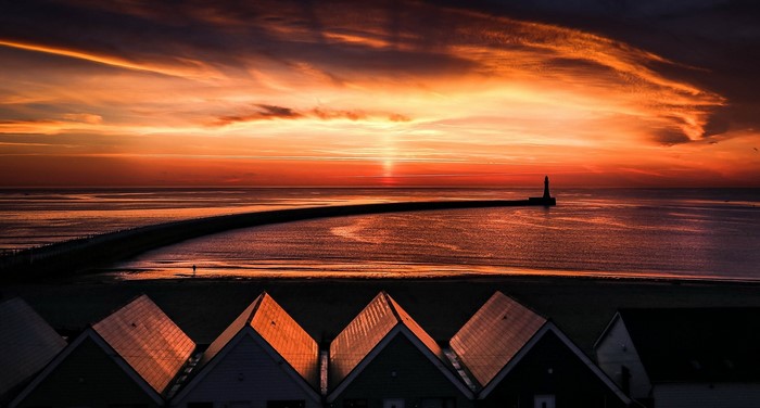 Sunset over the sea with a lighthouse and rooftops