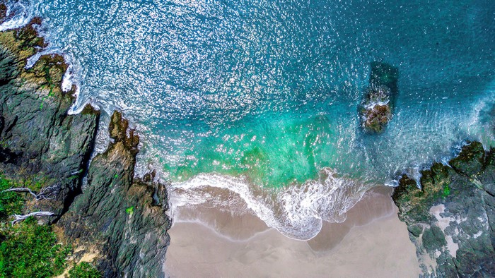 Aerial view of a rocky beach with turquoise waves
