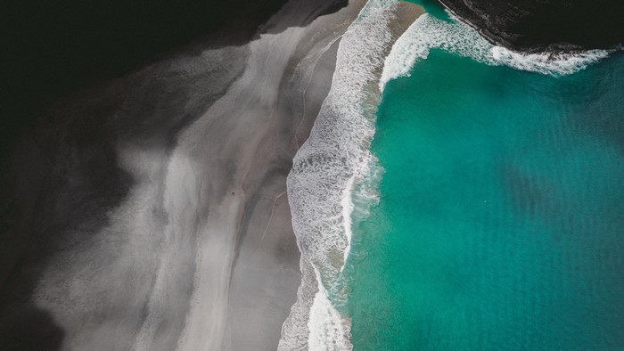Aerial view of a dark sand beach with turquoise waves