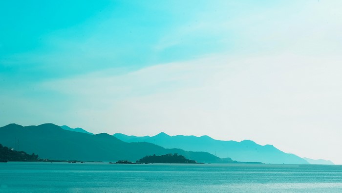 Turquoise ocean and distant mountains under a bright sky