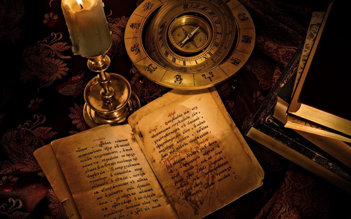 Candle, compass, books, and old papers on a patterned cloth
