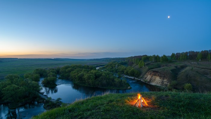 Campfire by the river at dusk with moon