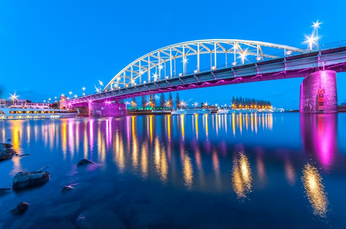 Bridge illuminated with purple and white lights over a river at dusk
