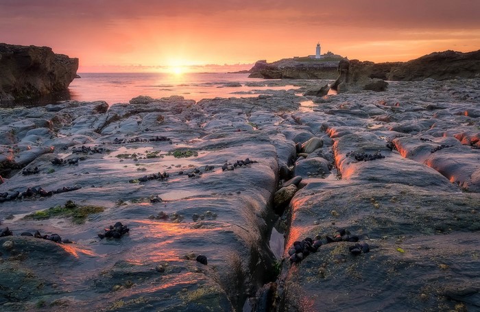 Sunset over rocky coast with lighthouse