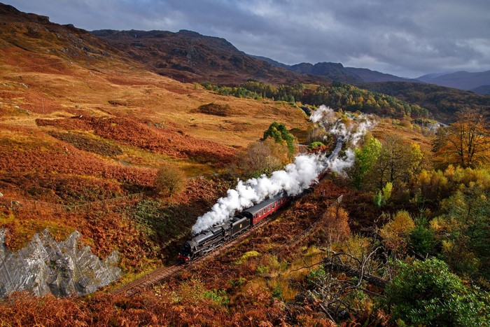 Steam train traveling through a Scottish landscape in autumn