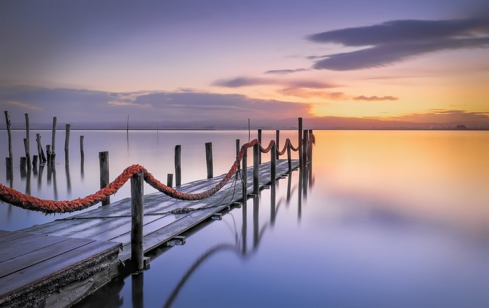 Wooden pier with rope railing at sunset over calm water