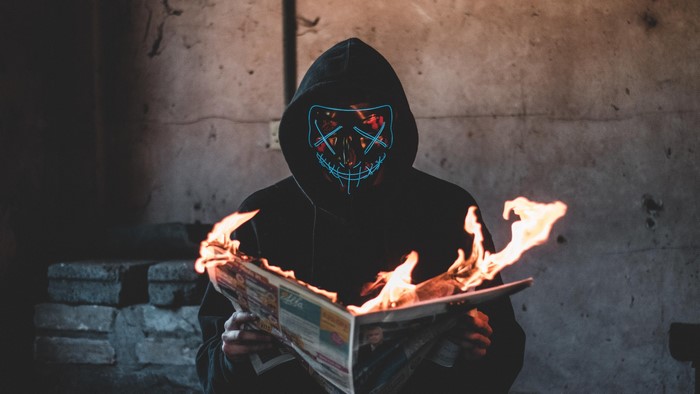 Person in neon mask burning newspaper
