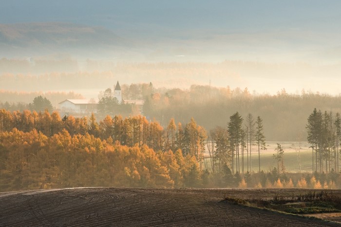 Misty autumn landscape with a church and fields