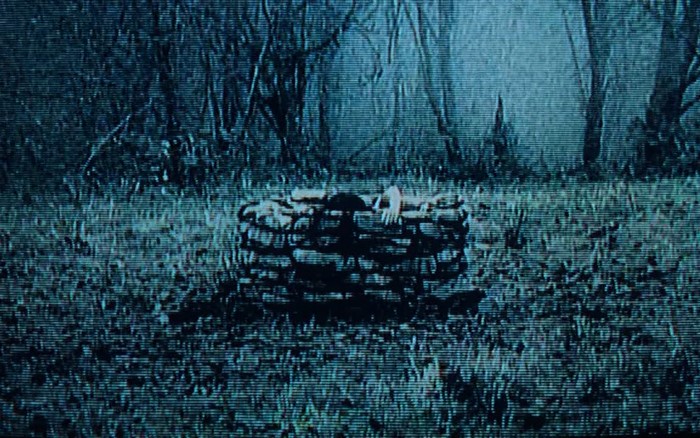 Woman crawling out of a well in a forest