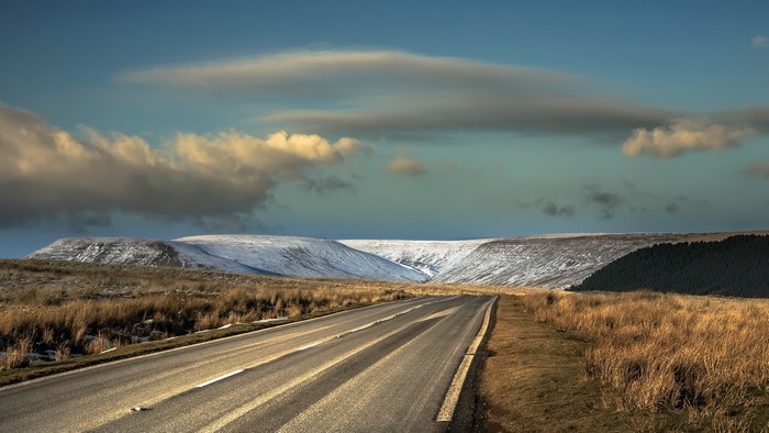Road through snowy hills under cloudy sky