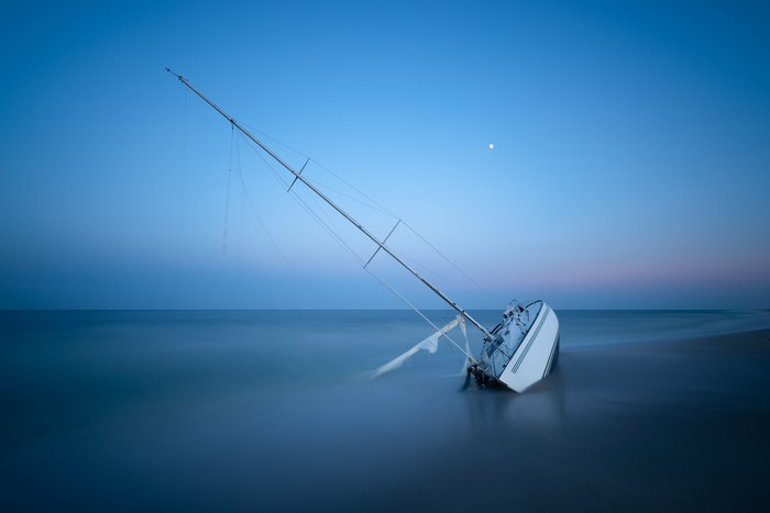 Shipwrecked sailboat on a beach at dusk