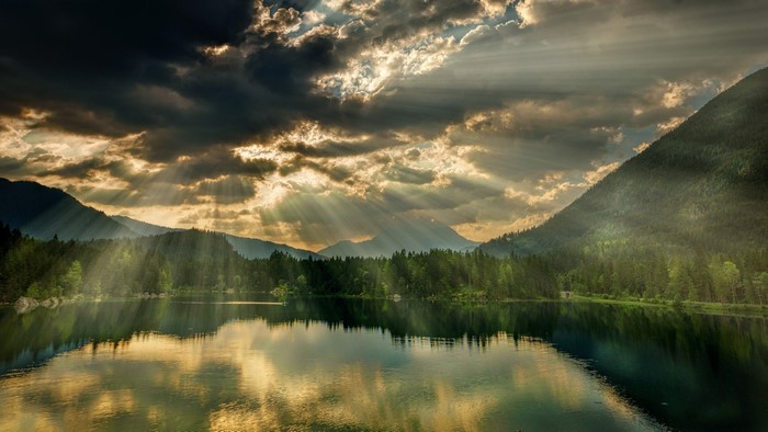 Sun rays over a forest lake and mountains