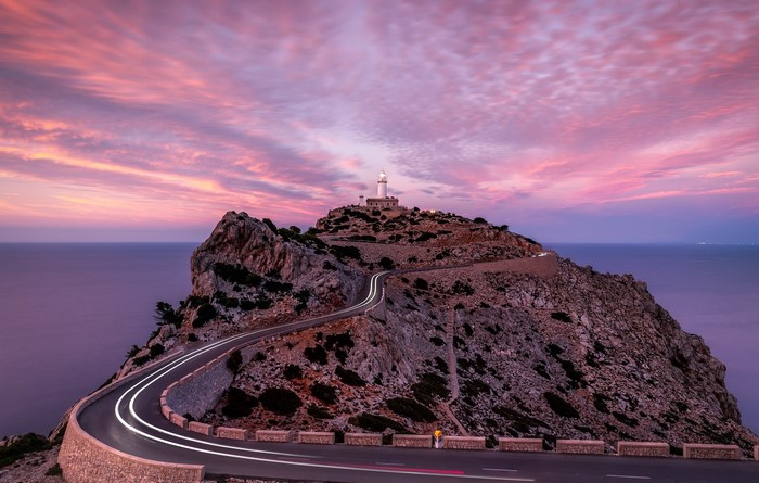 Lighthouse on a rocky cliff with a winding road at sunset