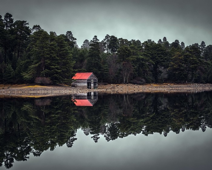 Wooden hut with red roof reflected in water