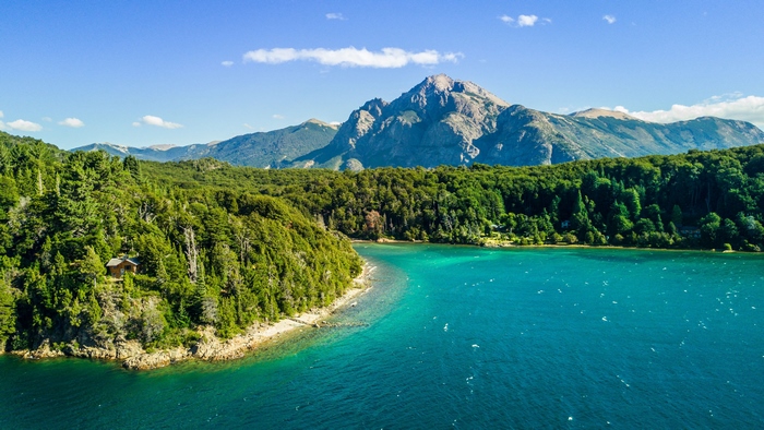 Turquoise lake and forested mountains with a cabin