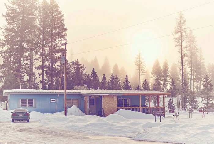 Blue house in a snowy forest with a car