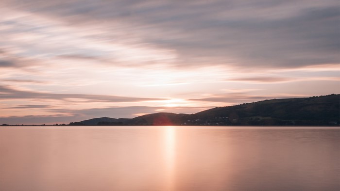 Sunset over calm water with hills