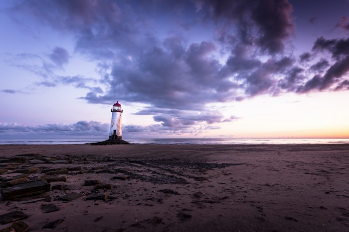 Lighthouse on a beach at sunset with clouds