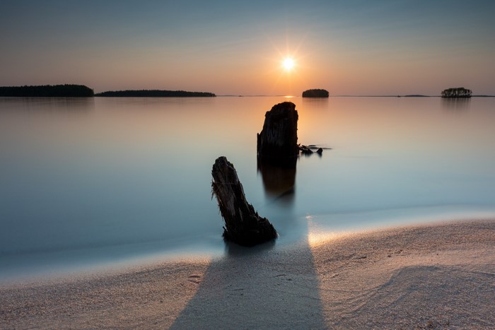 Sunset over calm water with wooden posts on a beach