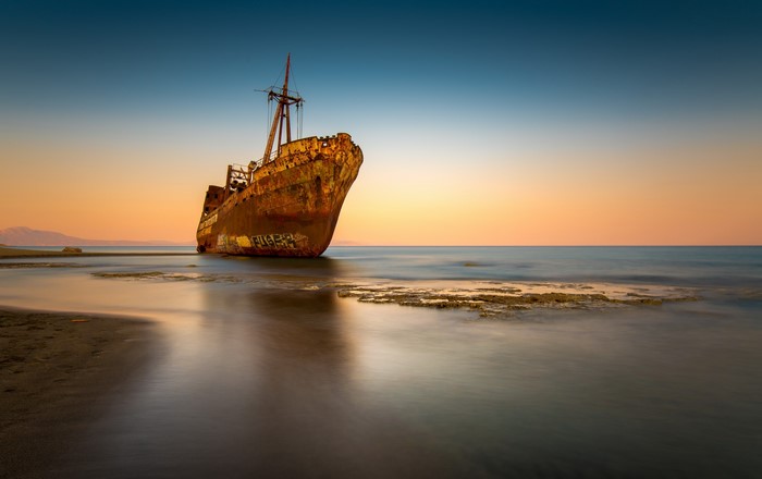 Rusty shipwreck on a beach at sunset