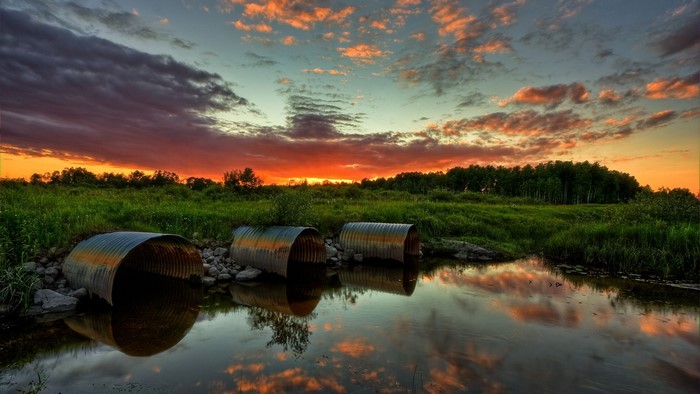 Sunset over a grassy field with pipes and water