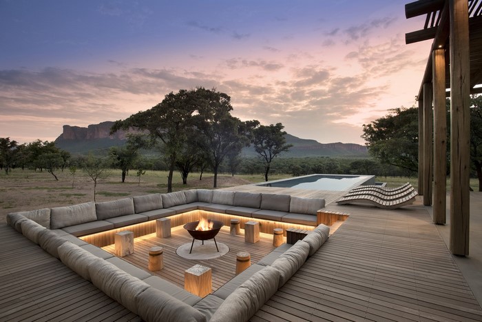 Outdoor lounge area with campfire and swimming pool at sunset