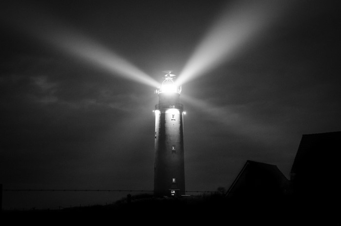 Monochrome night scene of a lighthouse with beams of light