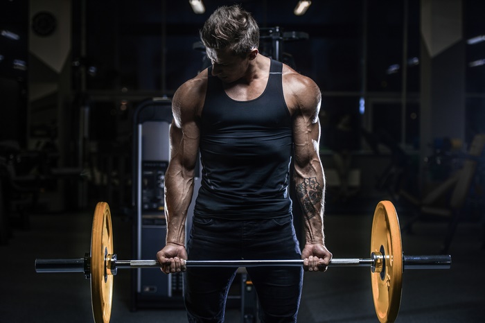 Bodybuilder performing barbell curls in a gym