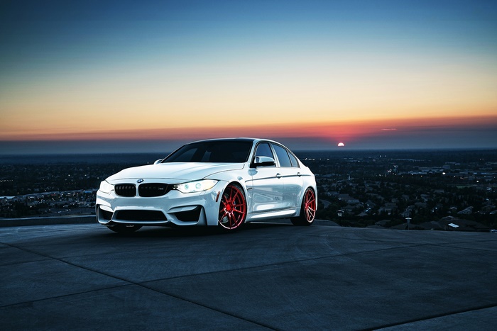 White BMW M3 sedan with red rims at sunset