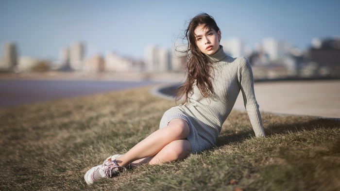 Brunette Woman Sitting on Grass with Cityscape
