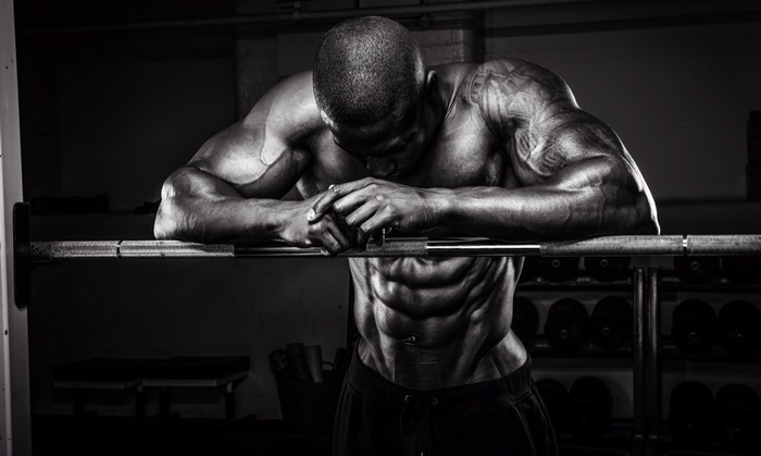 Muscular man resting on a barbell in a gym