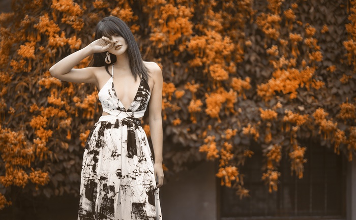 Asian woman in a patterned dress poses near orange flowers