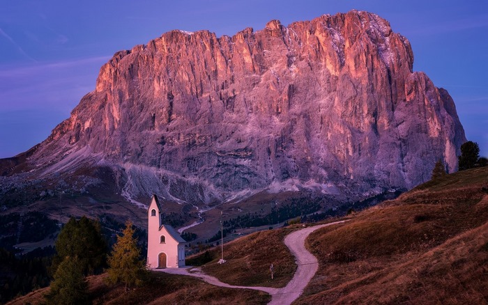 Small white church in front of a large mountain at sunset