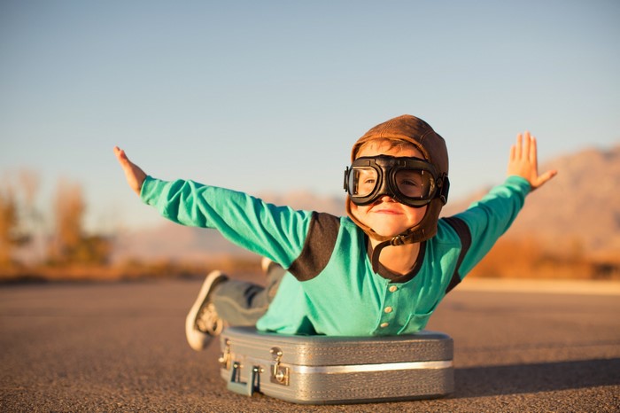 Boy in pilot goggles pretending to fly on a suitcase