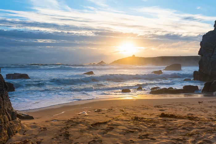 Ocean waves crash on a rocky beach at sunset