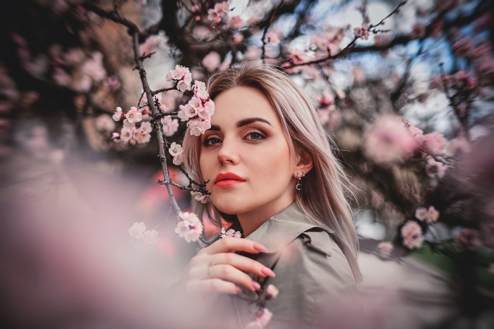 Woman with blonde hair and pink lipstick among blossoms