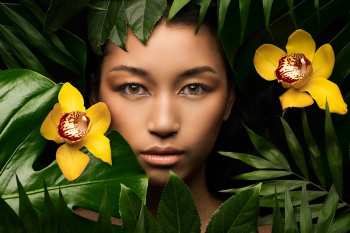 Woman's face surrounded by tropical leaves and orchids