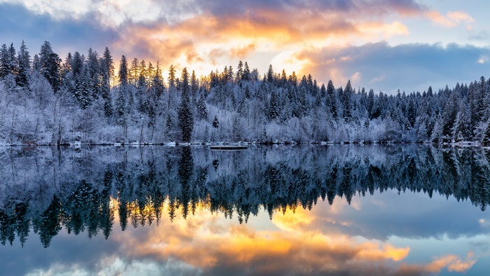 Snow-covered forest reflected in a lake at sunset