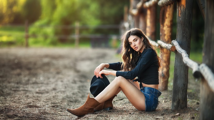 Woman in shorts and boots sitting by a fence