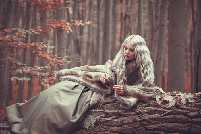 Woman in fur coat sitting on a log in forest