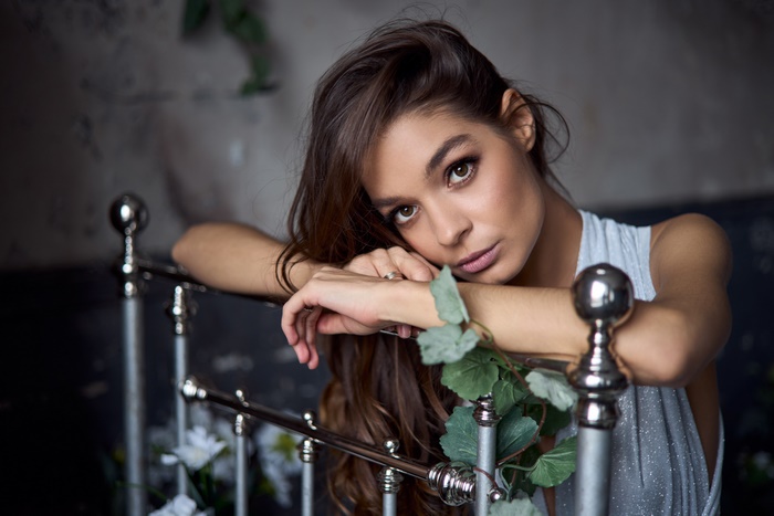 Woman with brunette hair leaning on a bed frame