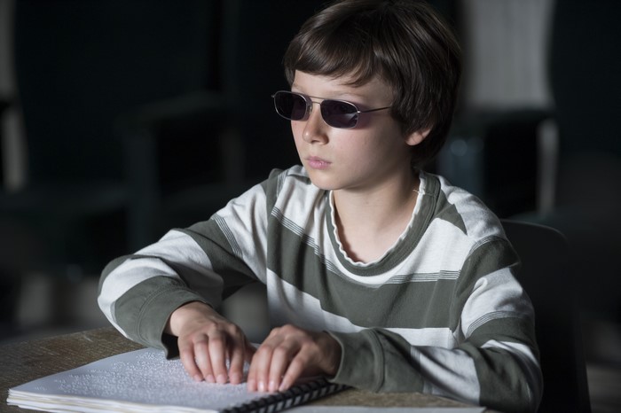 Boy wearing sunglasses reads Braille