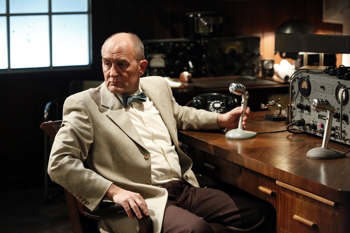 Agent Carter sits at a desk with a microphone