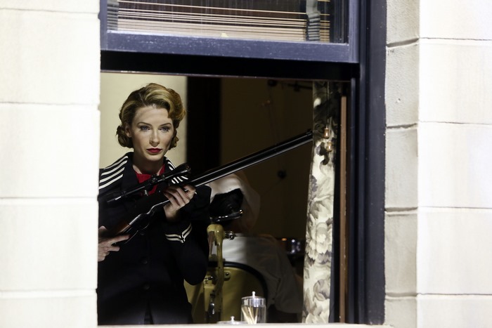 Woman with sniper rifle looking out window