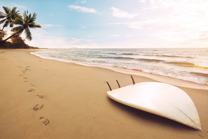 Surfboard on a sandy beach with palm trees and ocean